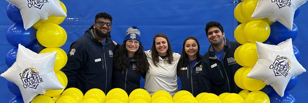 A group of students standing behind a "Welcome Chargers" balloon display.